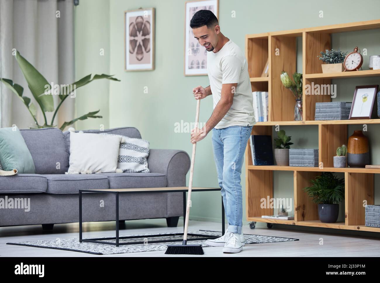Dust doesnt stand a chance in this house. Shot of a young man sweeping the floor at home. Stock Photo
