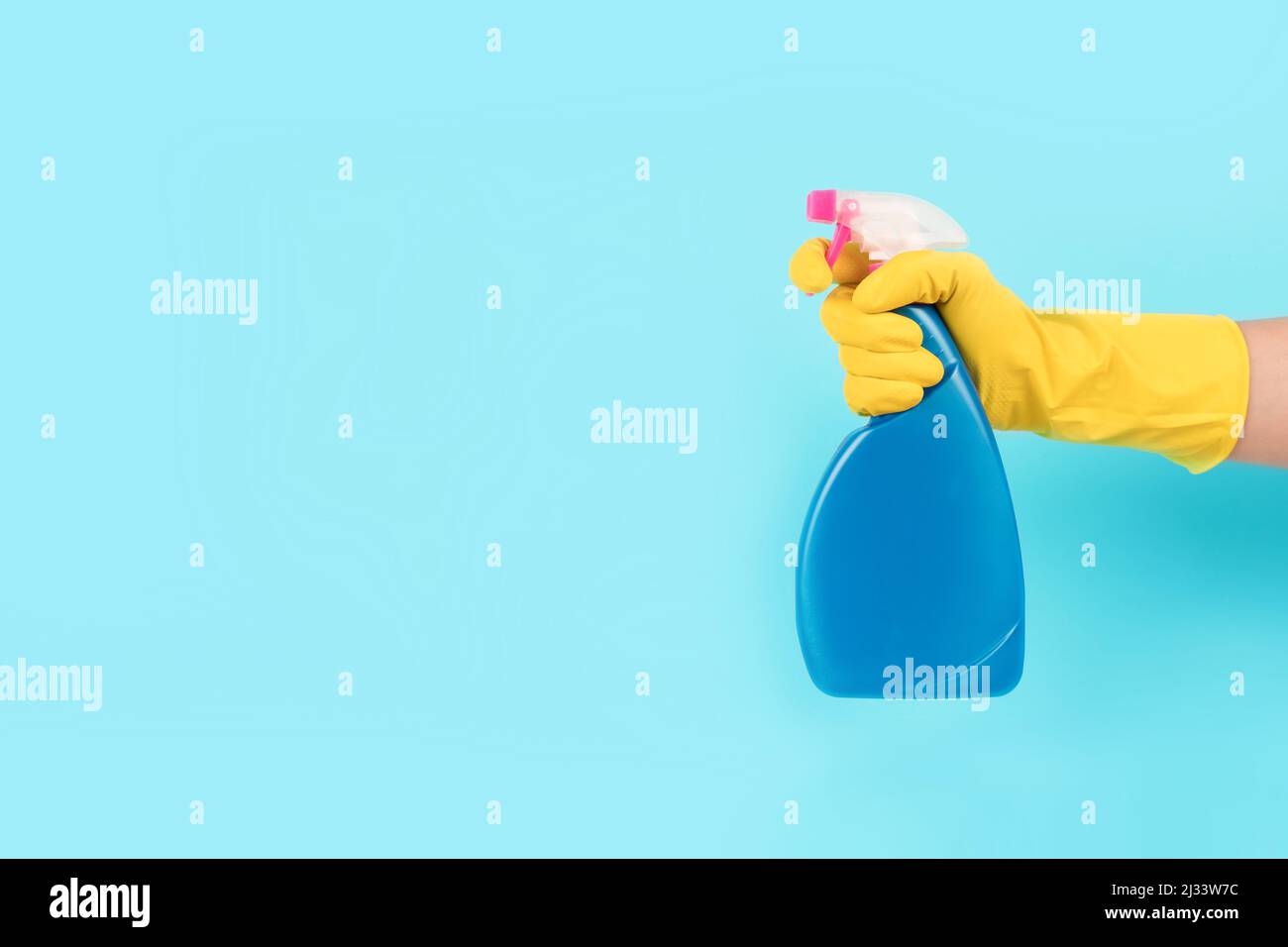 Hand in yellow protective rubber glove holding spray bottle with ...