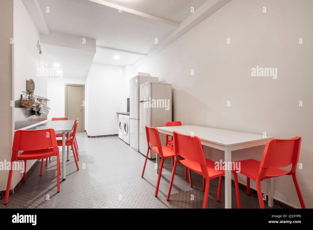 Open kitchen with two red dining tables and chairs, several refrigerators and two washing machines Stock Photo
