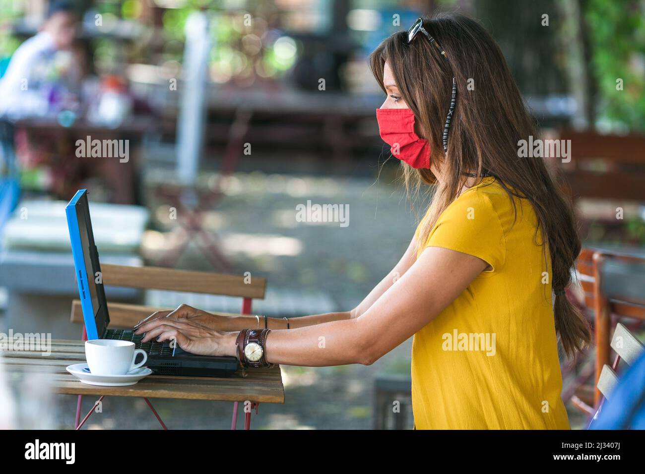 woman sitting in empty cafe wearing protecting mask working on laptop ...