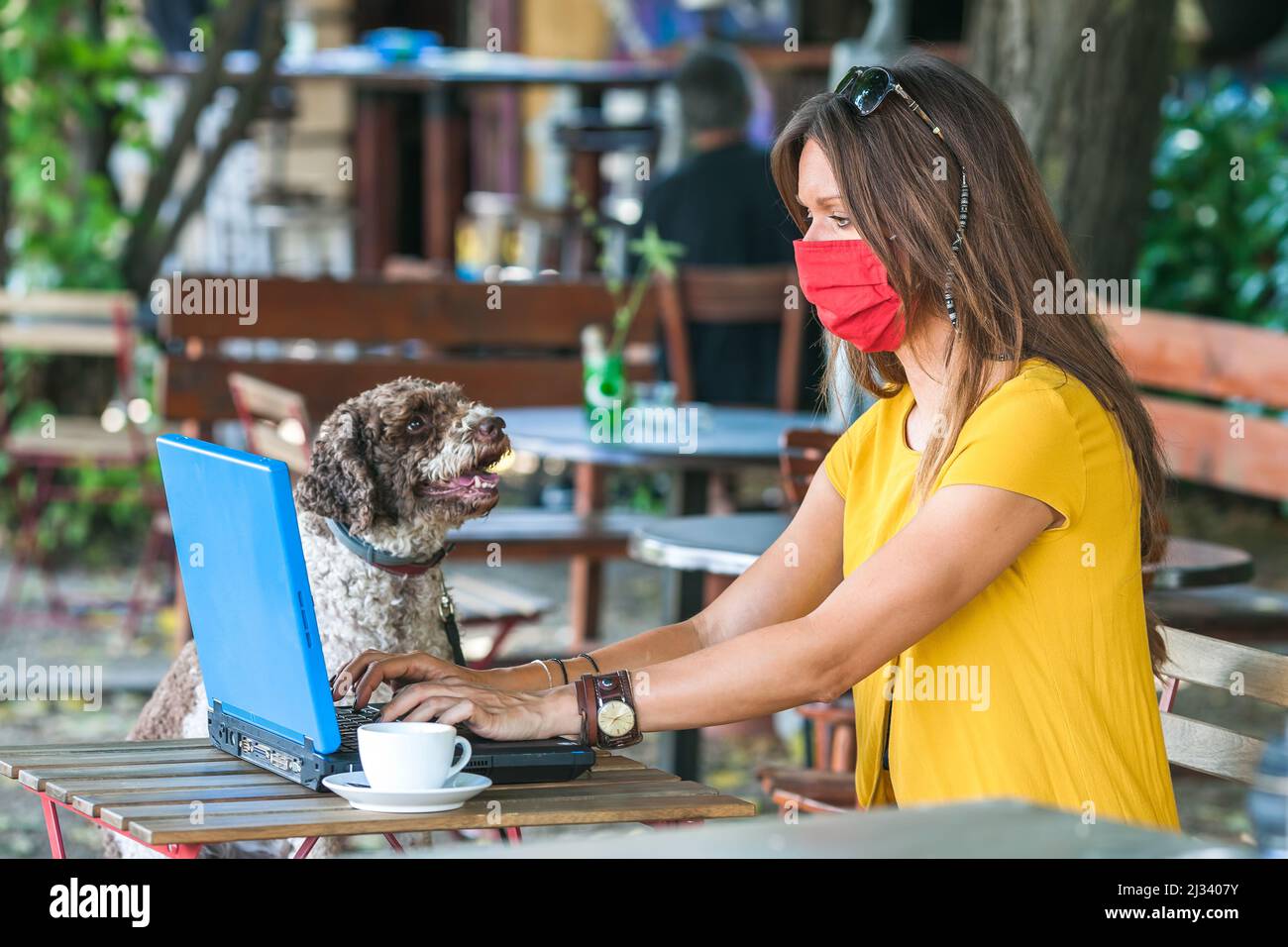 young woman sitting in empty cafe wearing face mask Stock Photo