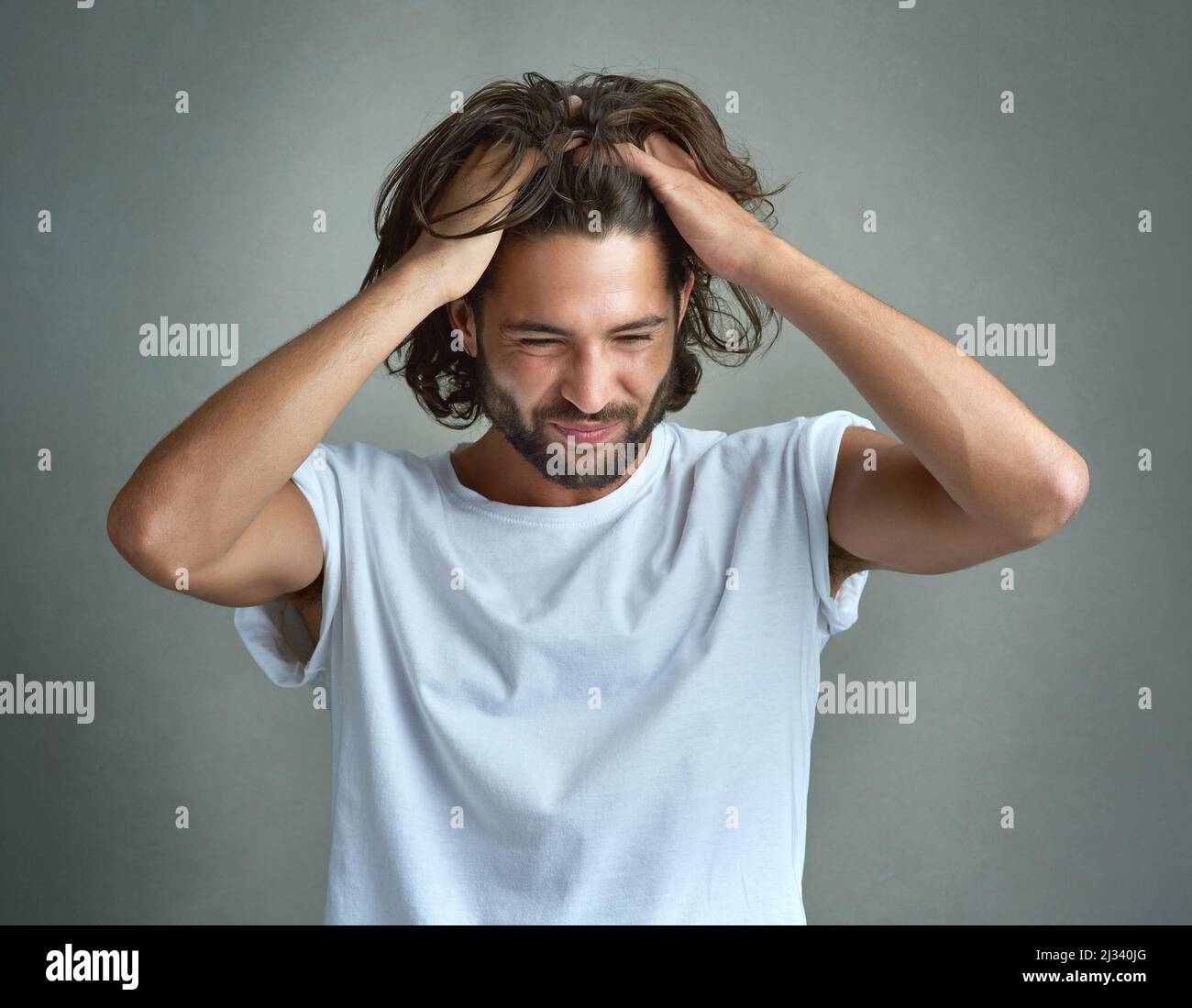 This is so frustrating. Studio shot of a young man looking upset against a grey background. Stock Photo