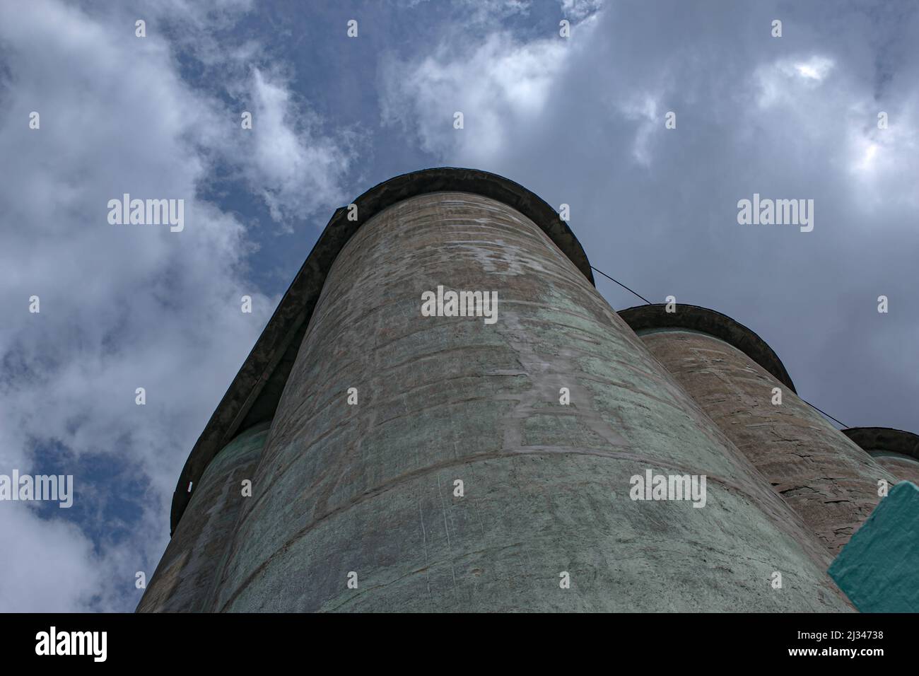 Grain elevator against a stormy sky. Large factory structure against a blue sky, low angle view. Stock Photo