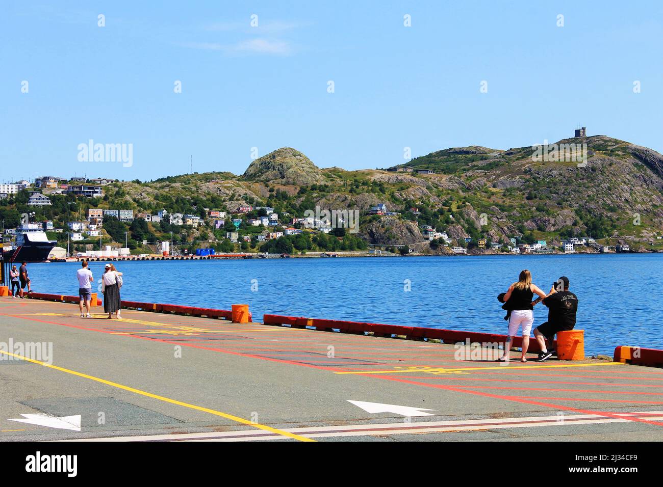People standing on the waterfront at St. John's Harbour, taking pictures of Signal Hill. Stock Photo