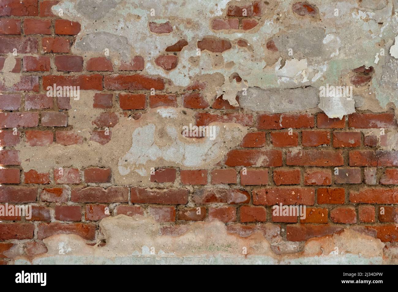 Broken red brick wall background texture with damaged plaster parts on it. Dirty rough surface of a building facade. Pattern of small weathered bricks Stock Photo