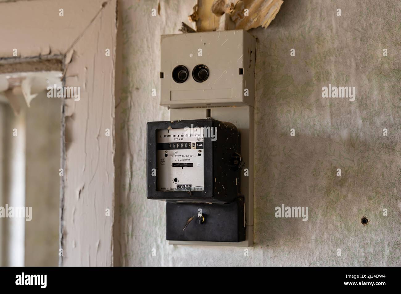 Old electric meter on a wall in an abandoned building. Electrical equipment to measure power consumption in a single room. Old vintage wallpaper Stock Photo