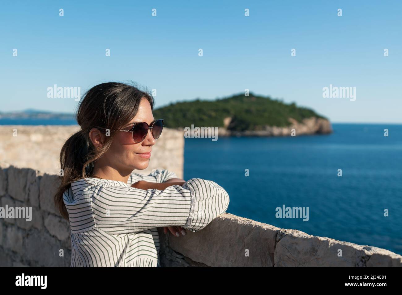 Woman looks out to sea from the city walls of the old town in Dubrovnik, Dalmatia, Croatia. Stock Photo