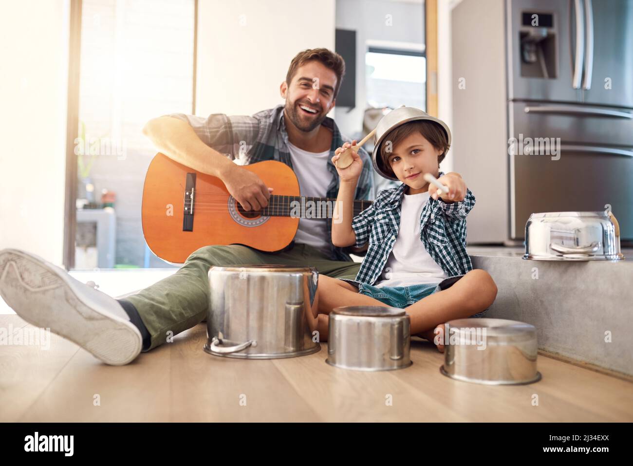 Are you ready for an encore. Portrait of a happy father accompanying his young son on the guitar while he drums on a set of cooking pots. Stock Photo