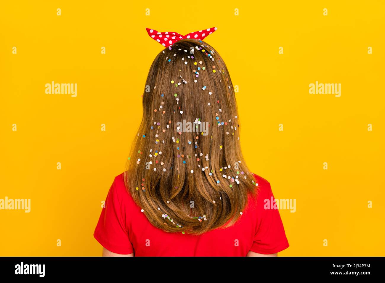 Back view photo of adorable charming little girl with long brown hair with confetti isolated on yellow color background Stock Photo