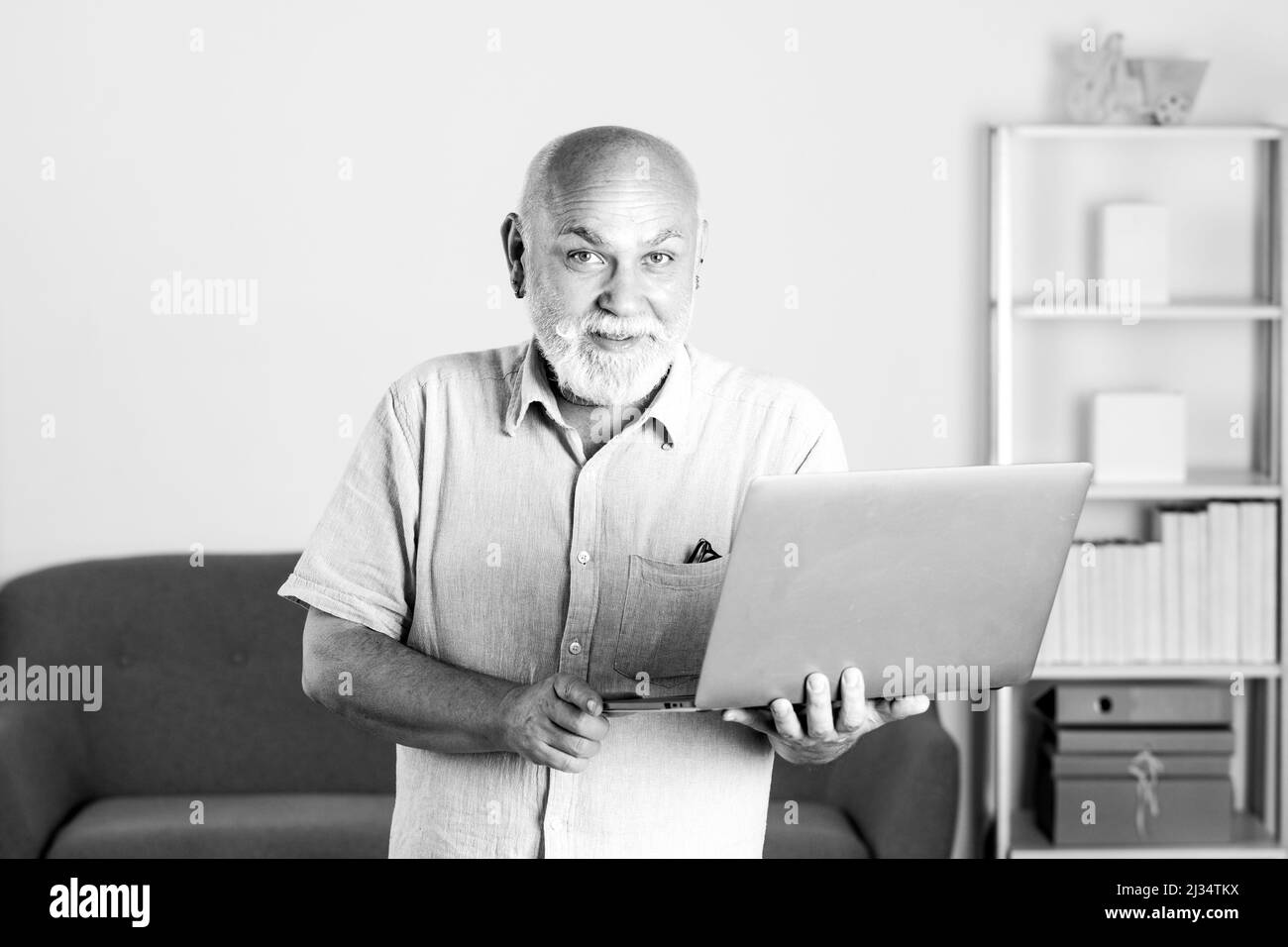 Grandfather, portrait of senior man with a laptop. Senior man with a gray beard at home. Mature man using computer. Stock Photo