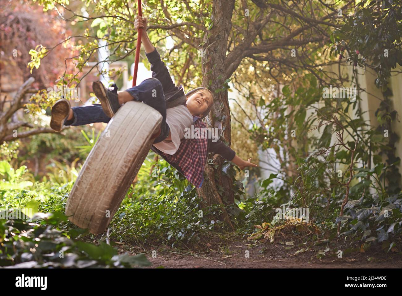 Carefree summer days of an idyllic childhood. A preteen boy swinging on a tyre swing in the garden. Stock Photo
