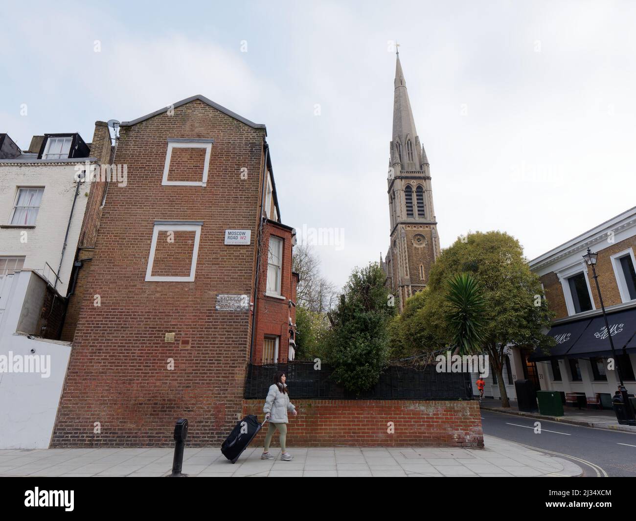 Woman with a rolling suitcase walks along Moscow Road in Bayswater with St Matthews Bayswater Church behind. London Stock Photo