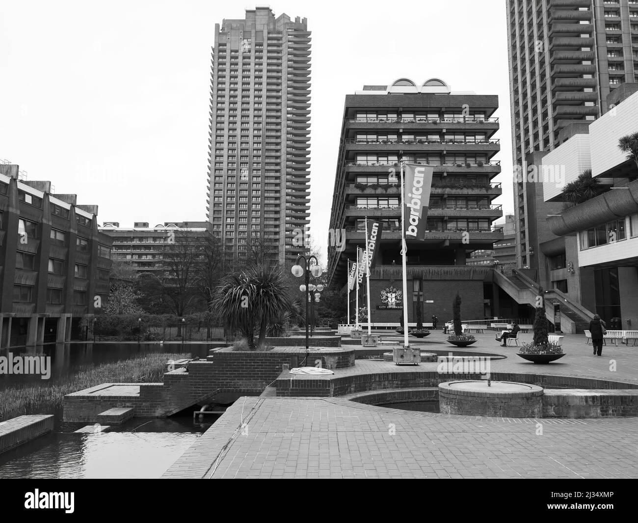 London, Greater London, England, March 29 2022: Part of the Barbican complex with high rise buildings and a courtyard seated area. Monochrome. Stock Photo