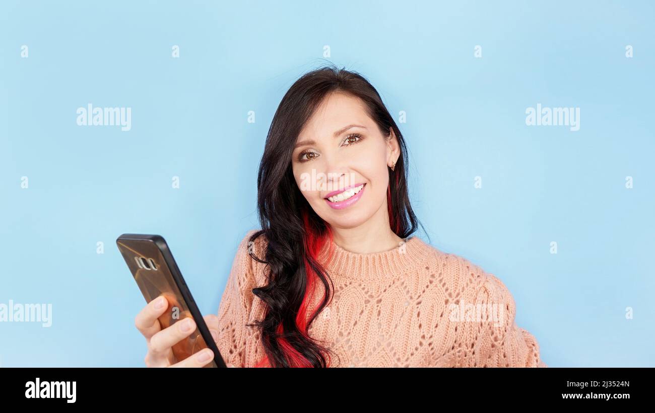 Photo of pretty excited lady curly brunette with red hair smiling hold telephone post youth blog read comments wear coral pullover isolated blue color Stock Photo