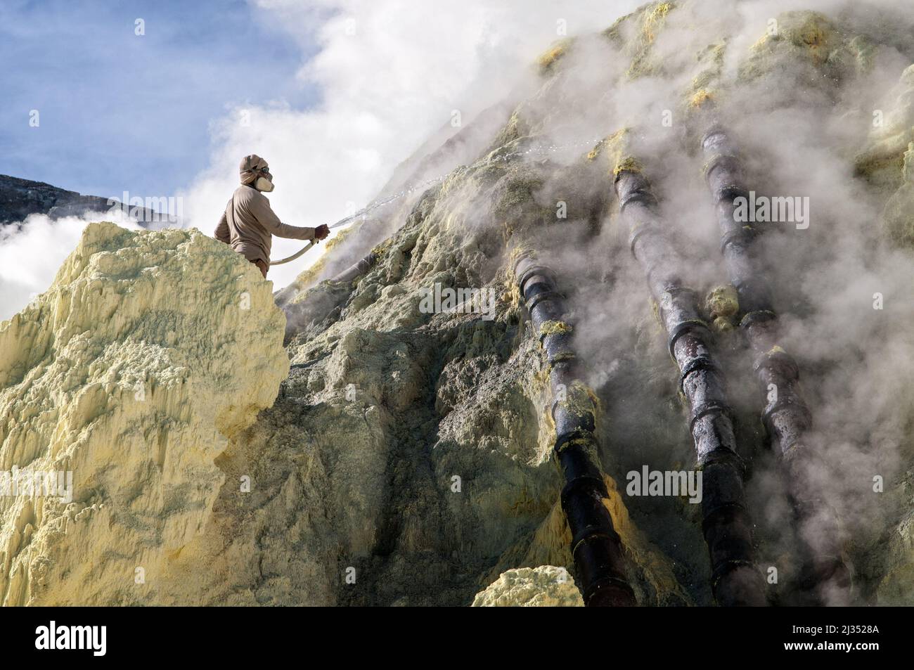 Miner cooling pipes by spraying water on them inside the crater of Ijen volcano, Java island, Indonesia Stock Photo