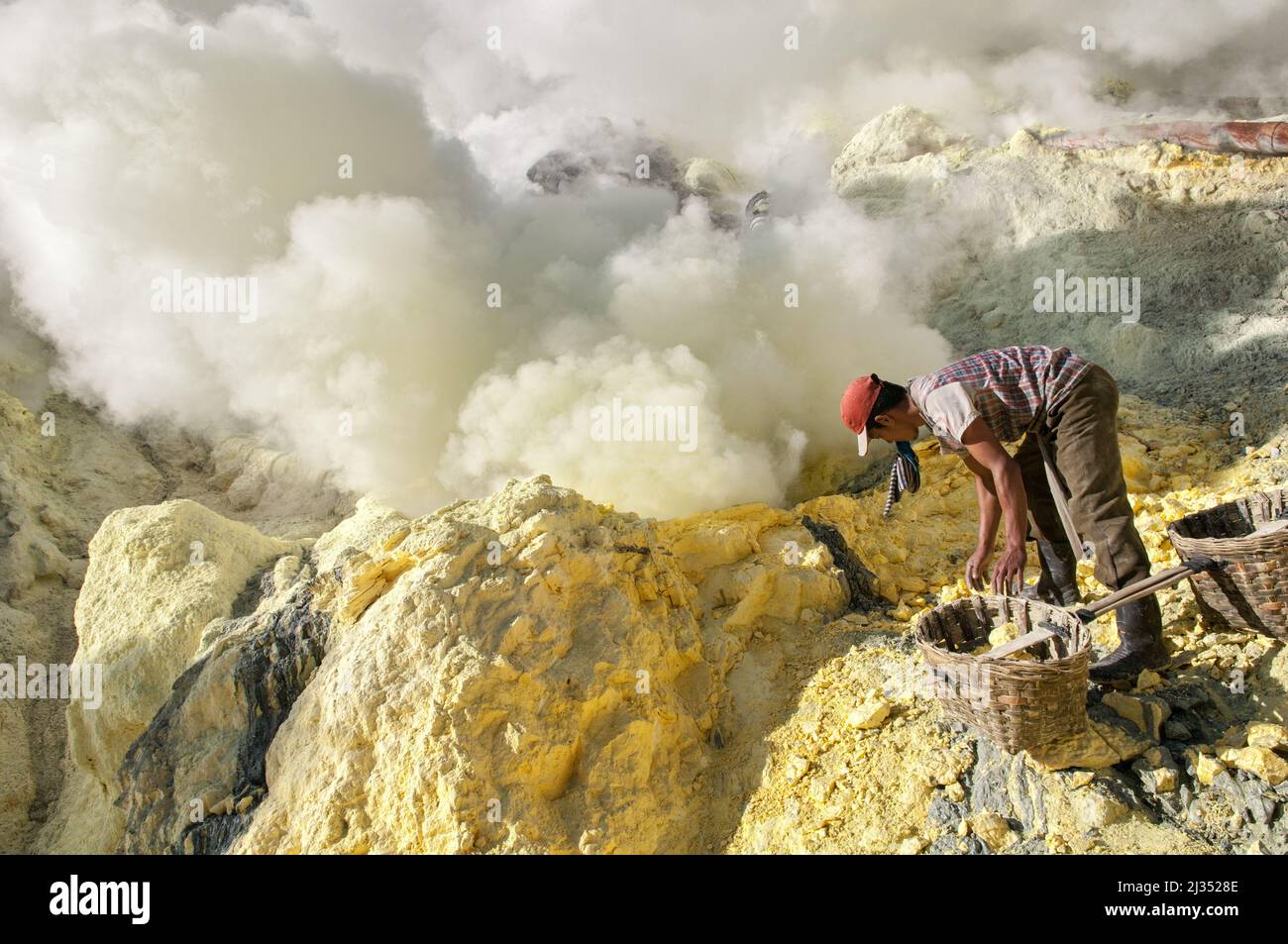 Miner filling his baskets with sulfur inside the crater of Ijen volcano, Java island, Indonesia Stock Photo
