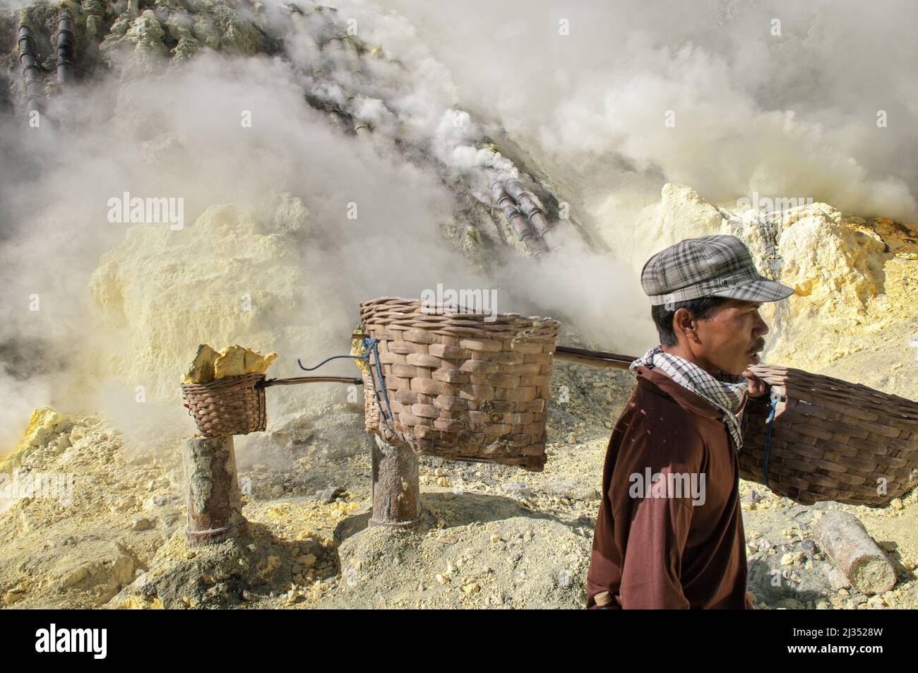 Sulfur miner and baskets inside the crater of Ijen volcano, Java Island, Indonesia Stock Photo