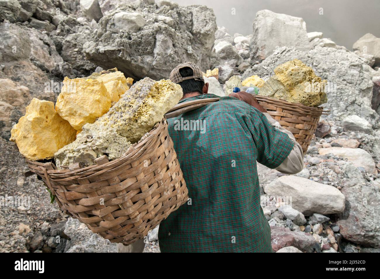 Miner carrying heavy baskets with sulfur from the crater of Ijen volcano, Java Island, Indonesia Stock Photo