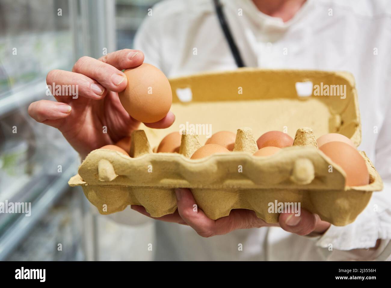 Hand holding a cardboard box with organic local eggs while shopping in the supermarket Stock Photo