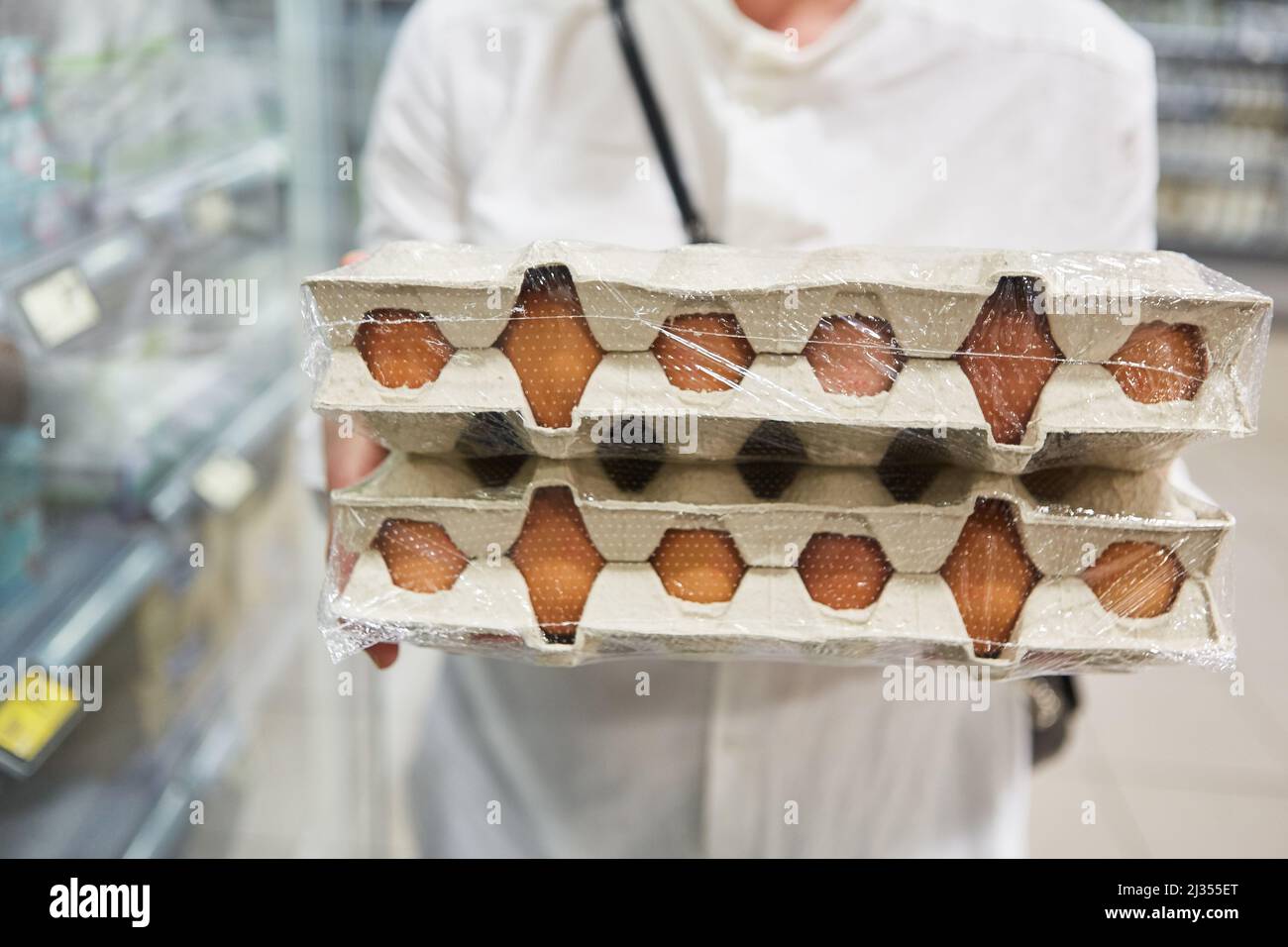 Customer carries stack of organic egg cartons while shopping in supermarket Stock Photo