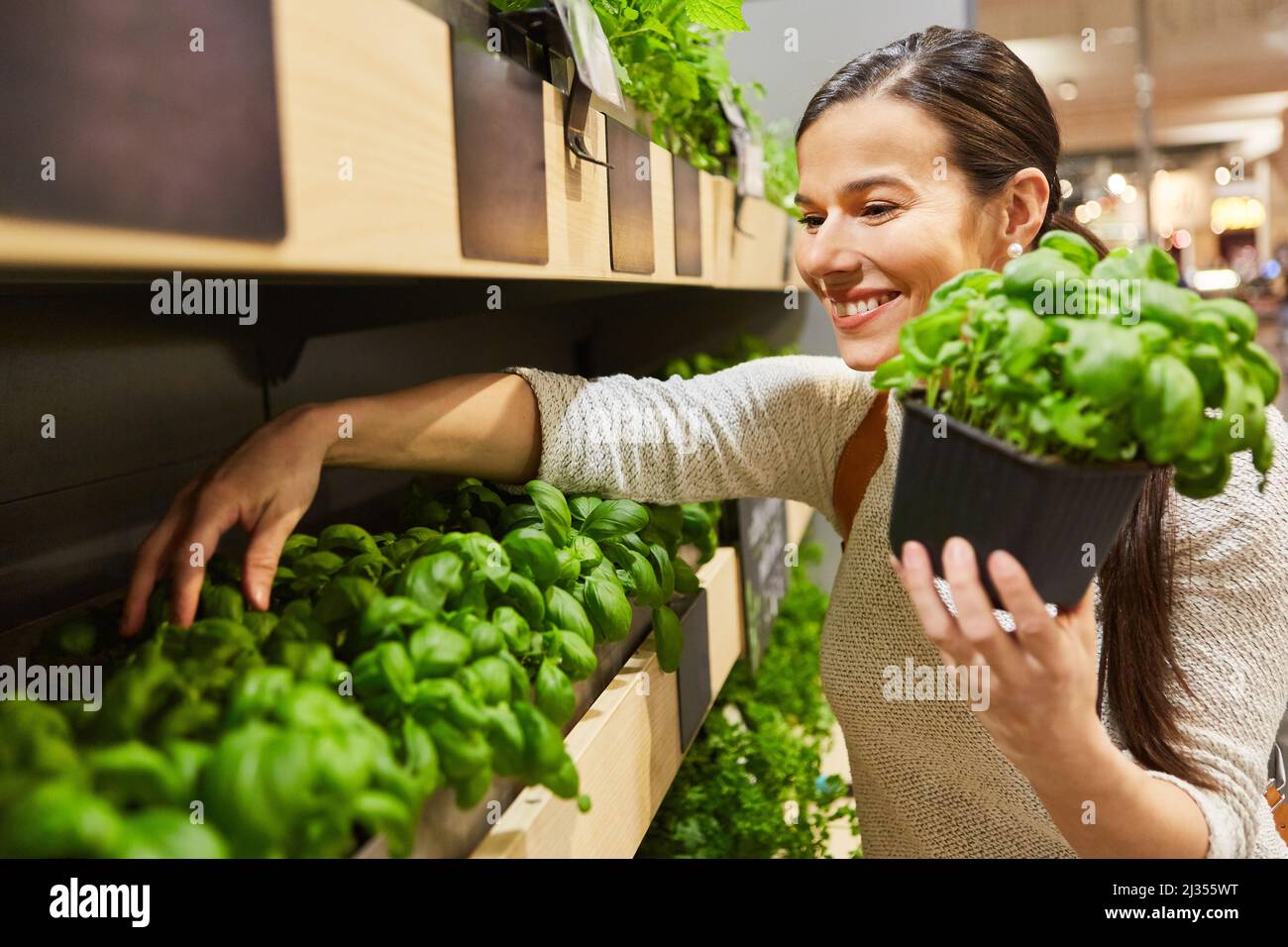 Young woman as a smiling customer at the herb shelf buys basil in the supermarket Stock Photo