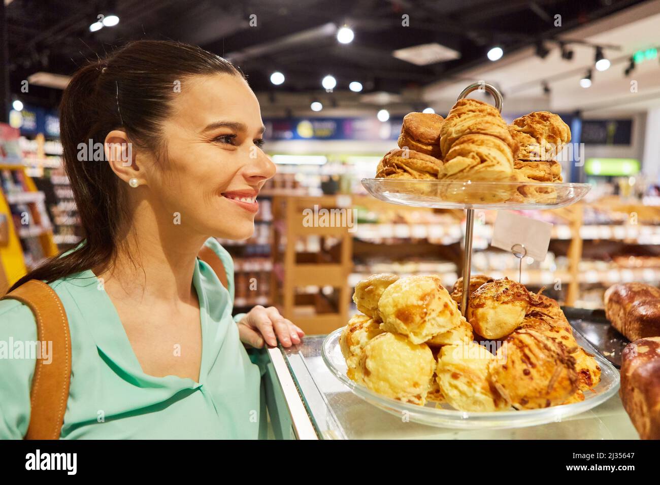 Young woman as a smiling customer looks at a shelf with a selection of baked goods in the supermarket Stock Photo