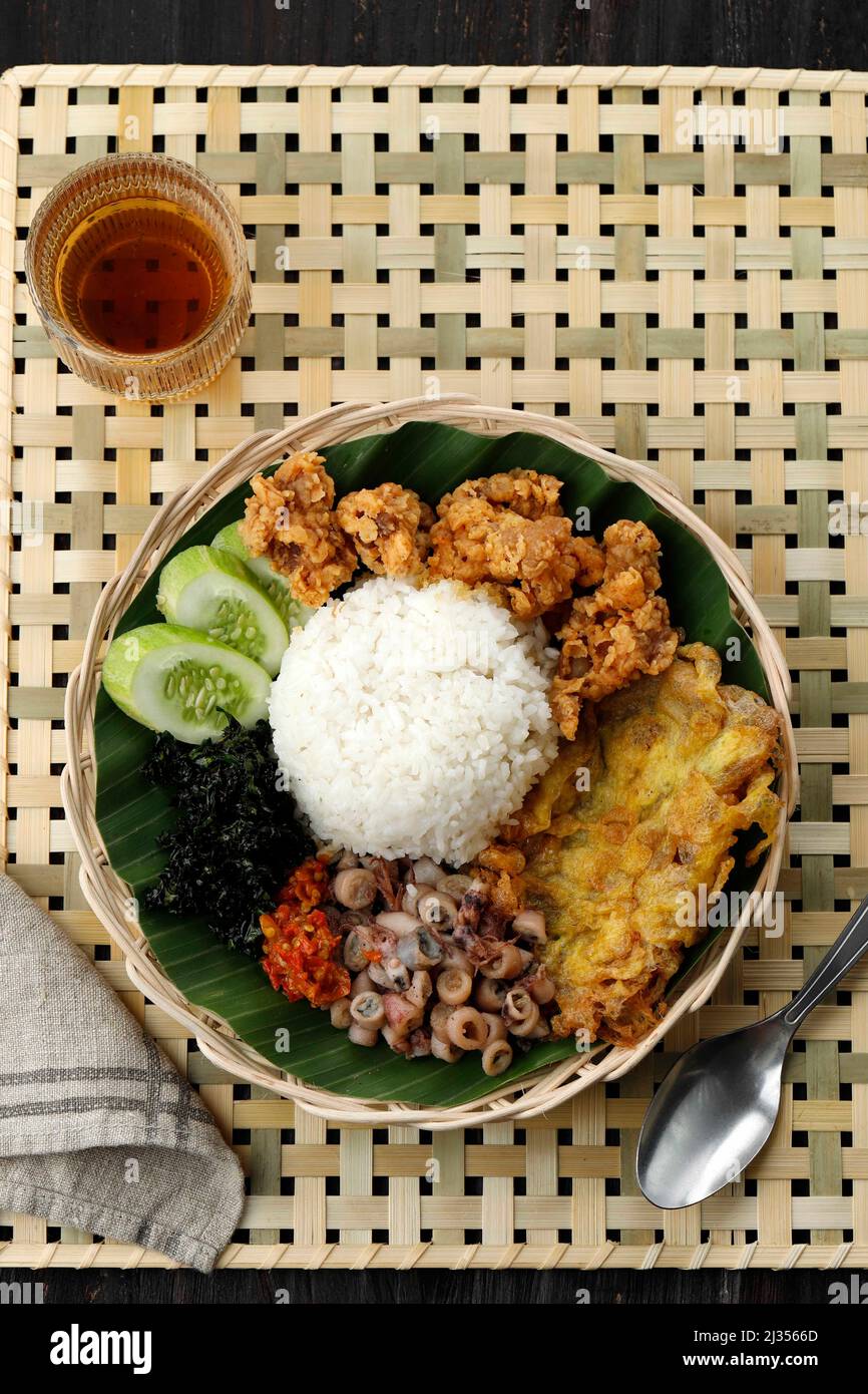 Top View Nasi Campur Cumi Asin, White Rice with Sautee Salted Squid, Sambal, Egg, Kulit Ayam Crispy Chicken Skin, and Boiled Cassava Leaf. Stock Photo