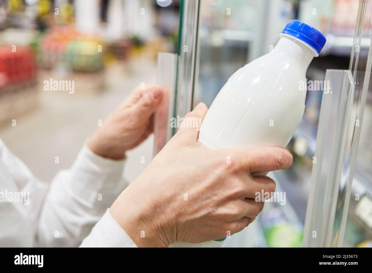 Hand holding a bottle of milk or almond milk on the refrigerated shelf