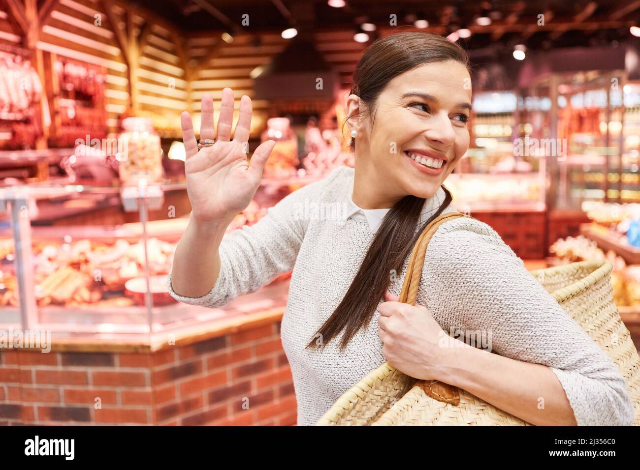 Smiling woman as happy customer with shopping bag in supermarket waving Stock Photo