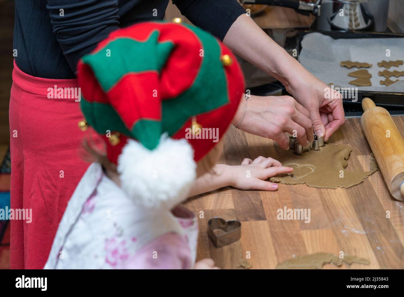 Mother in her thirties and her three year old daughter wearing a Christmas hat, making gingerbread men together out of dough at Christmas. England Stock Photo