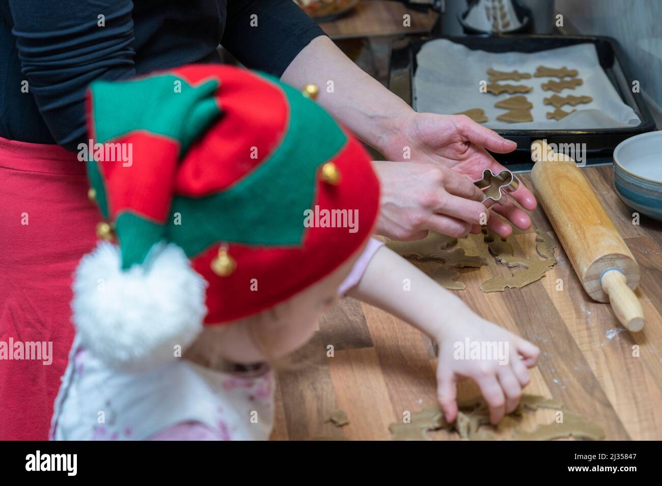 Mother in her thirties and her three year old daughter wearing a Christmas hat, making gingerbread men together out of dough at Christmas. England Stock Photo