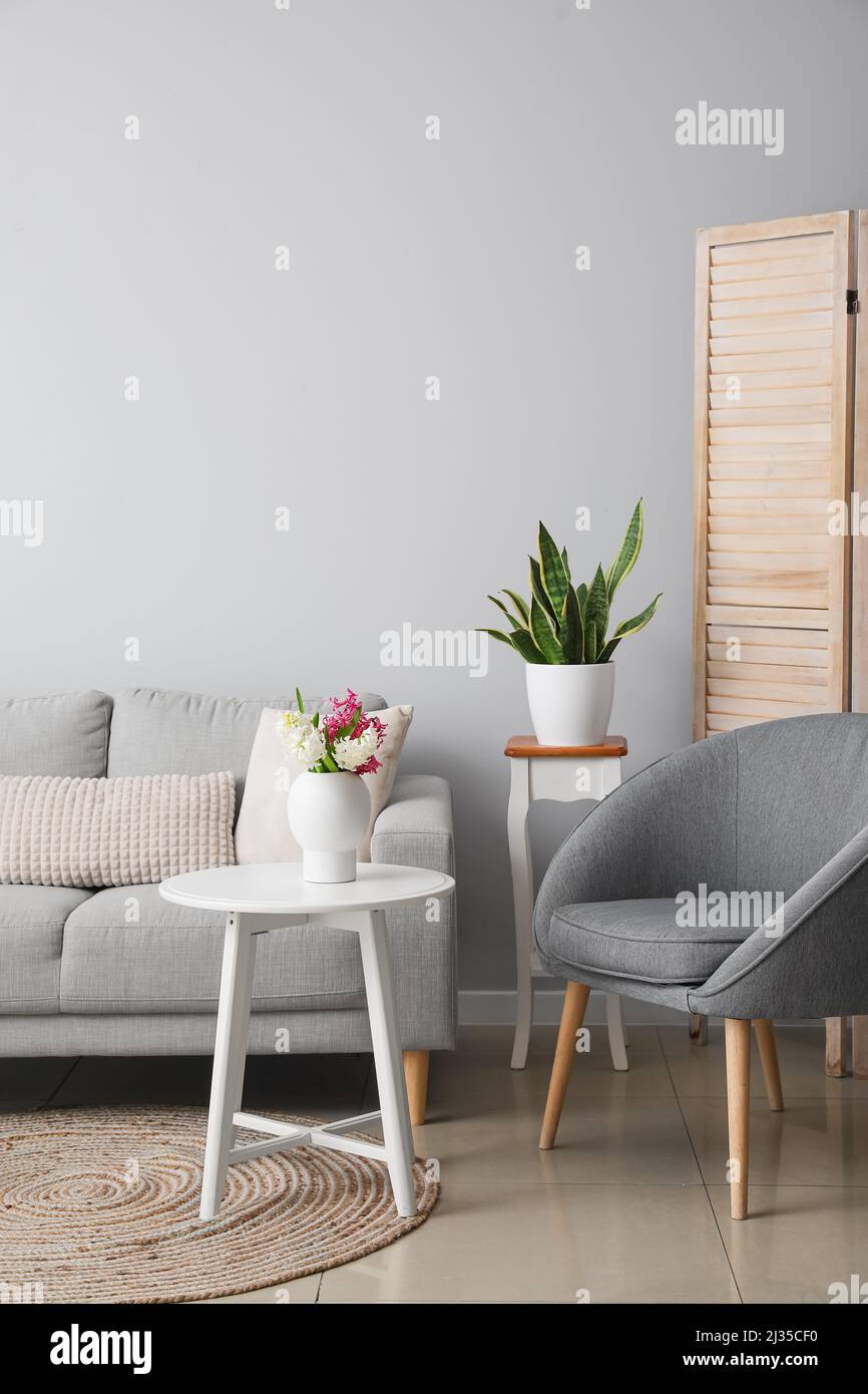Interior of modern living room with grey sofa, armchair and flowers in