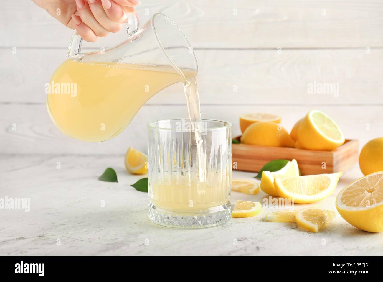 Woman pouring lemon juice from jug into glass on table Stock Photo Alamy