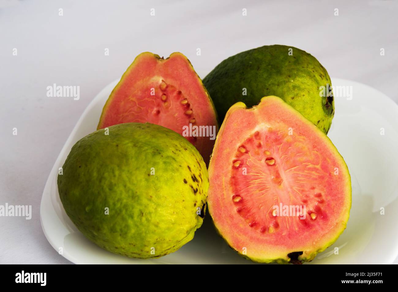 Halves of a red guava on a white plate between two whole guavas with