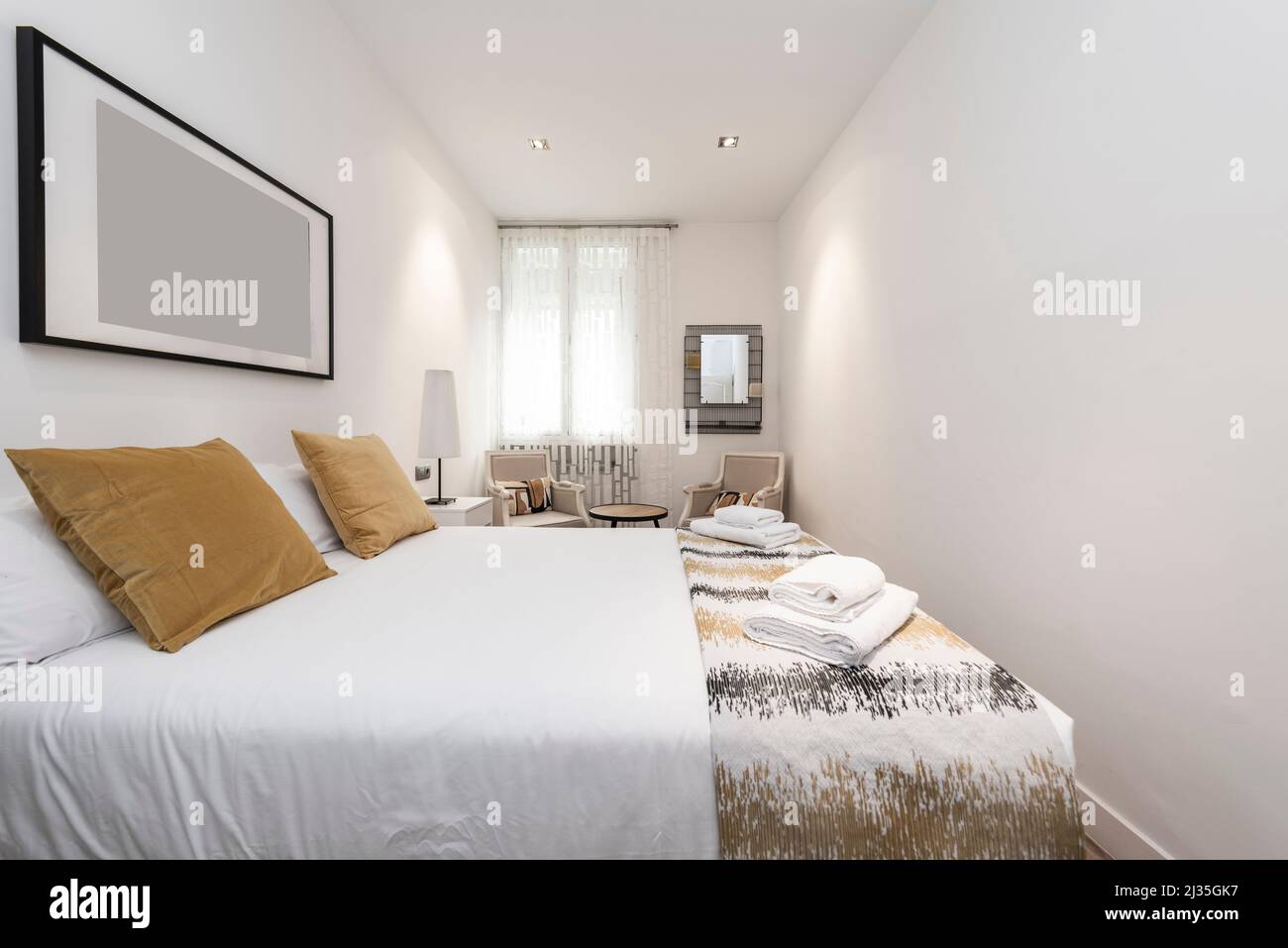Bedroom with a large double bed with golden cushions, armchairs and towels on the bed in a vacation rental apartment Stock Photo
