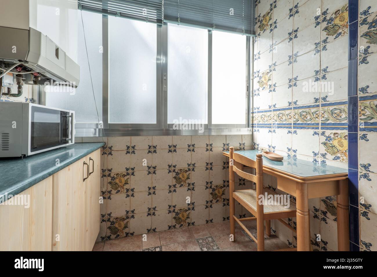 tiled kitchen with super kitsch tiles and wooden table with chair against the wall Stock Photo