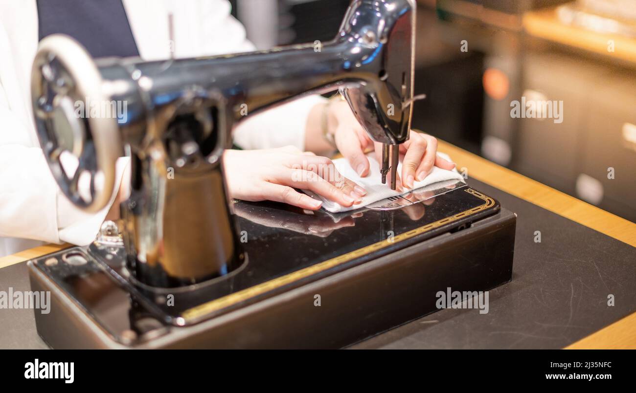 Female hand using vintage sewing machine scribbling fabric and repairing the cloth at home. Stock Photo