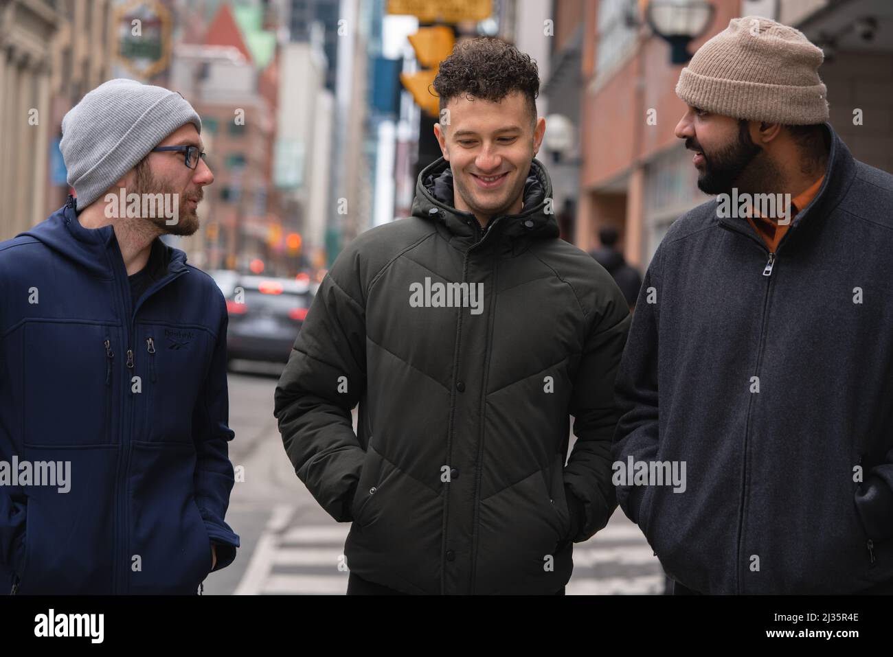 Group of interracial adult male friends talking and smiling together having conversation in the streets of downtown Toronto, Ontario Canada Stock Photo