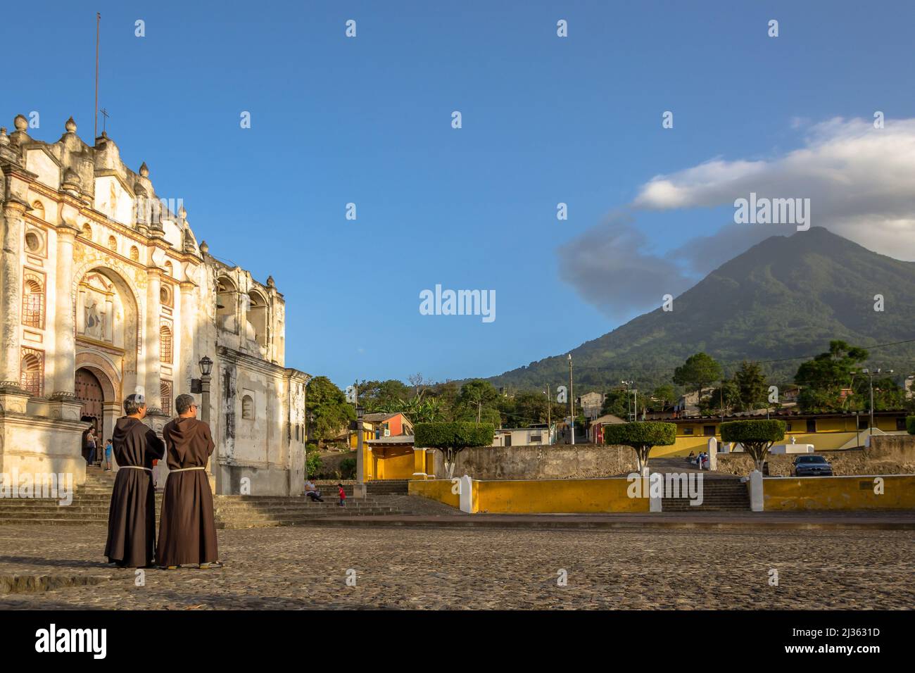 Two Franciscans catholic priests staring at Agua volcano during sunset at San Juan del Obispo church, just before going to mass. Stock Photo