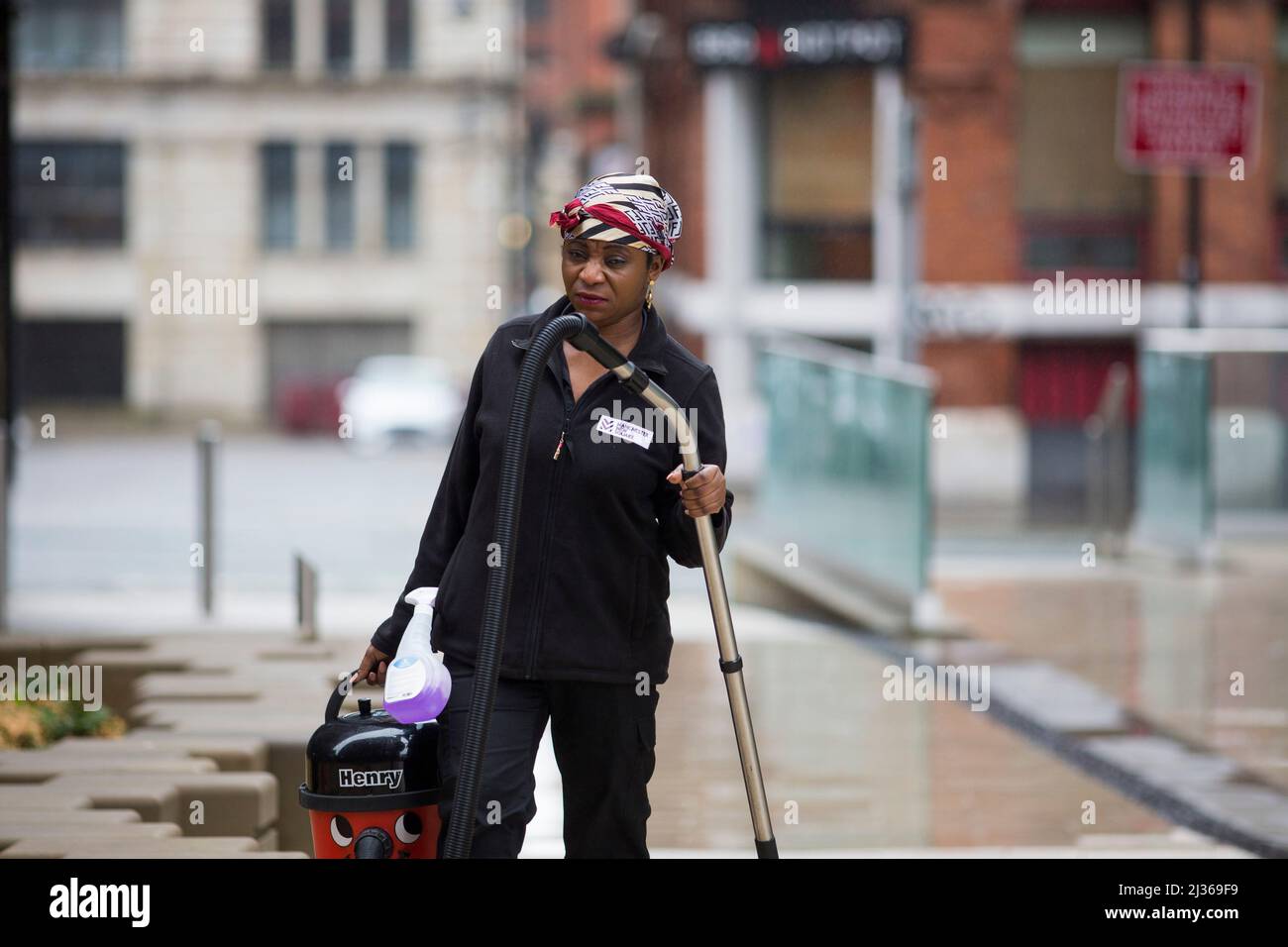A women of ethnic origin carrying a Henry hoover in a mixed development of flats and offices in Manchester city centre wearing a headscarf. Stock Photo