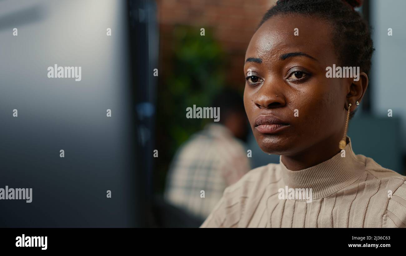 African american software programer working focused looking at computer screen and smiling while typing in it startup office. System engineer coding with algorithms compiling on screens in background. Stock Photo