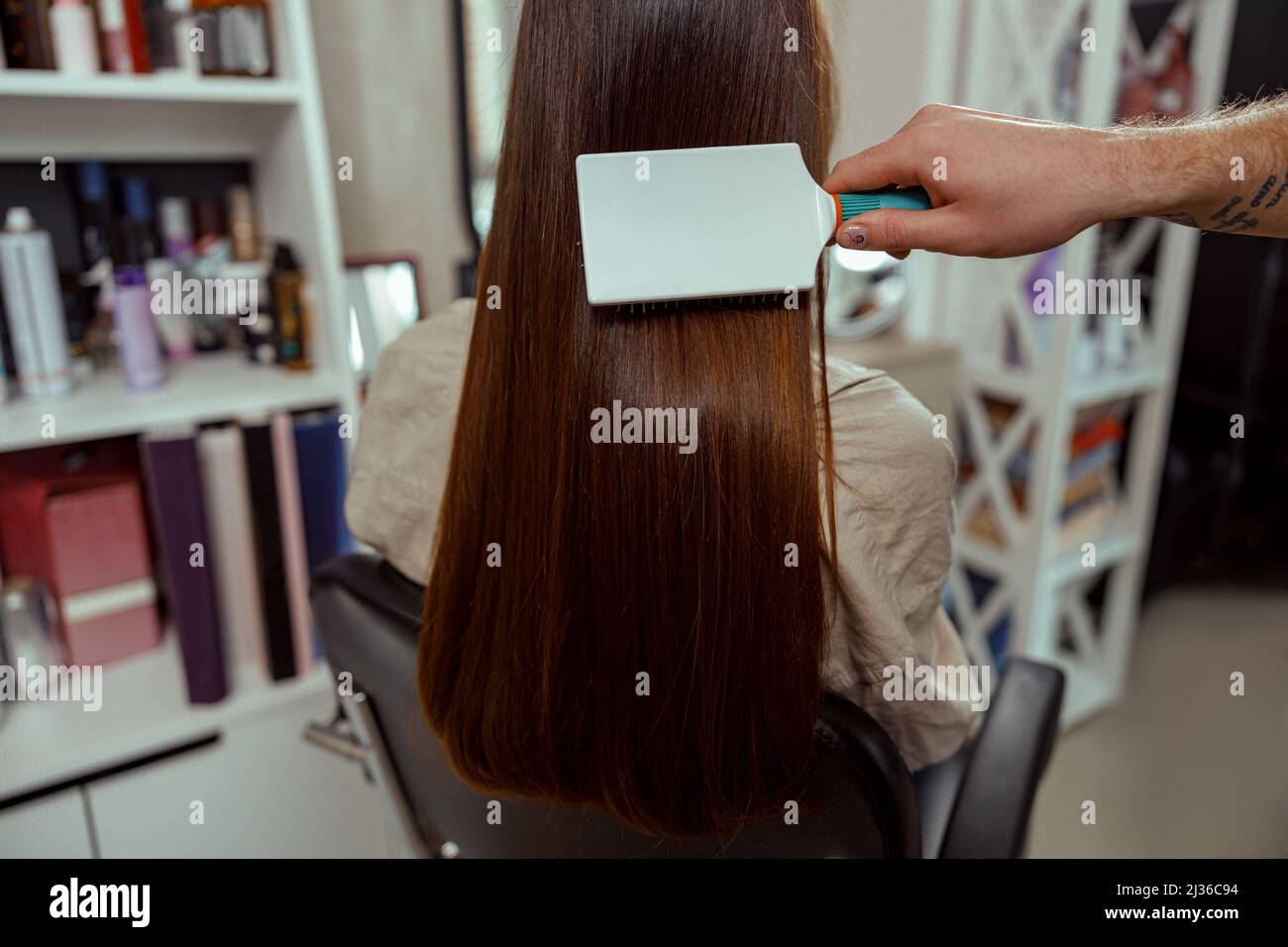 Closeup of hairstylist brushing long and sleek brown hair of female client at beauty salon Stock Photo