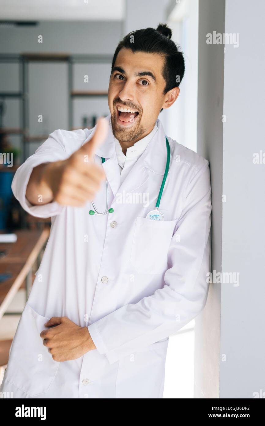 Vertical portrait of cheerful male doctor in white medical uniform ...