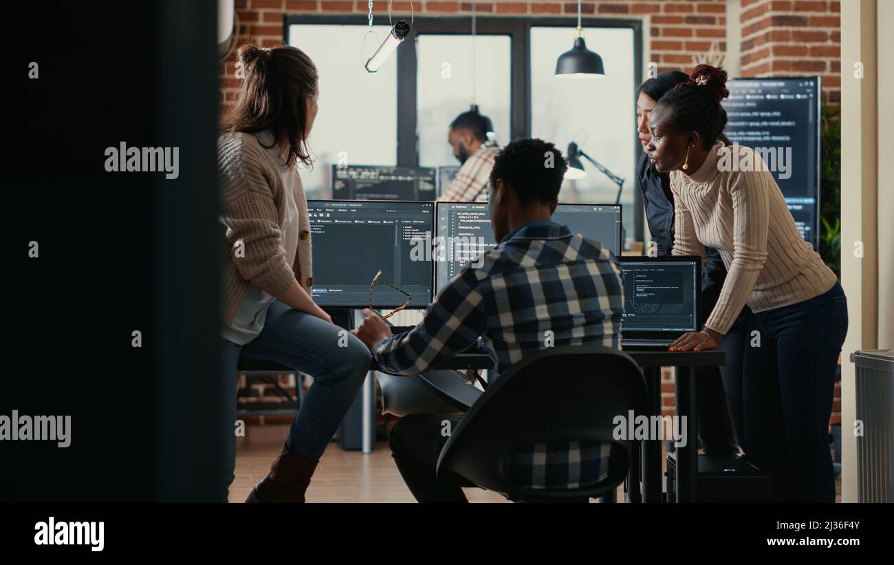 Software programmers discussing about online cloud computing while the rest of the team joins in front of multiple screens compiling code. Coders doing teamwork looking at running algorithms. Stock Photo