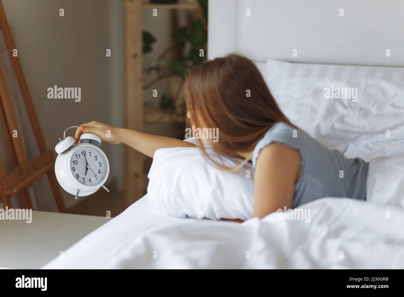 Woman sleep on the bed turns off the alarm clock wake up at the morning, Selective focus.Young woman reaching to turn off alarm clock ,early morning Stock Photo