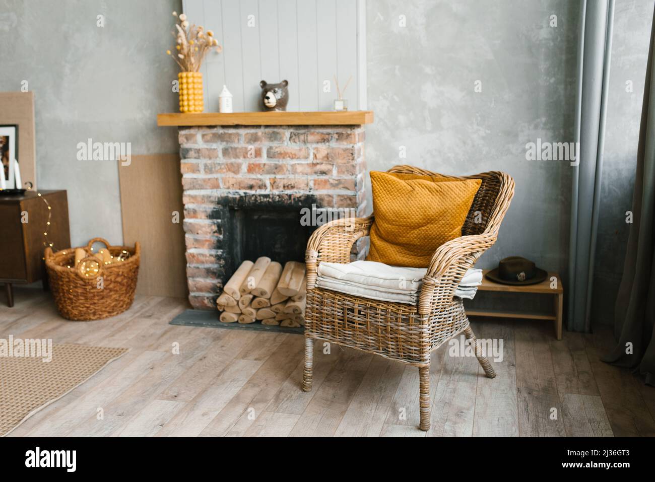 A wicker armchair with a yellow cushion near a brick fireplace with firewood, a children's wooden toy wheelchair in the Scandinavian-style living room Stock Photo