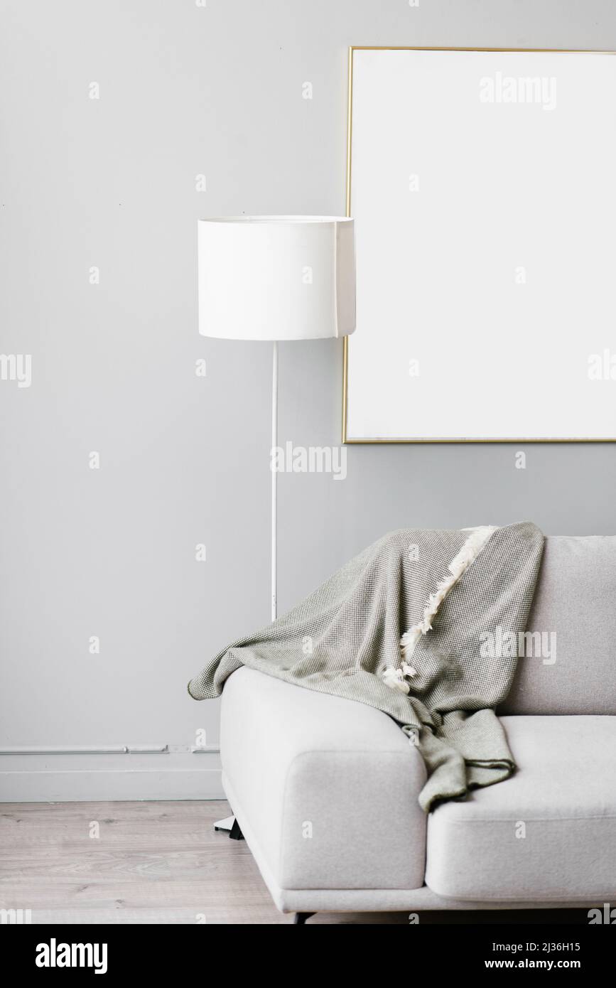 Stylish minimalistic interior of the living room in gray. Sofa with plaid, floor lamp and mockup white frame on the wall Stock Photo