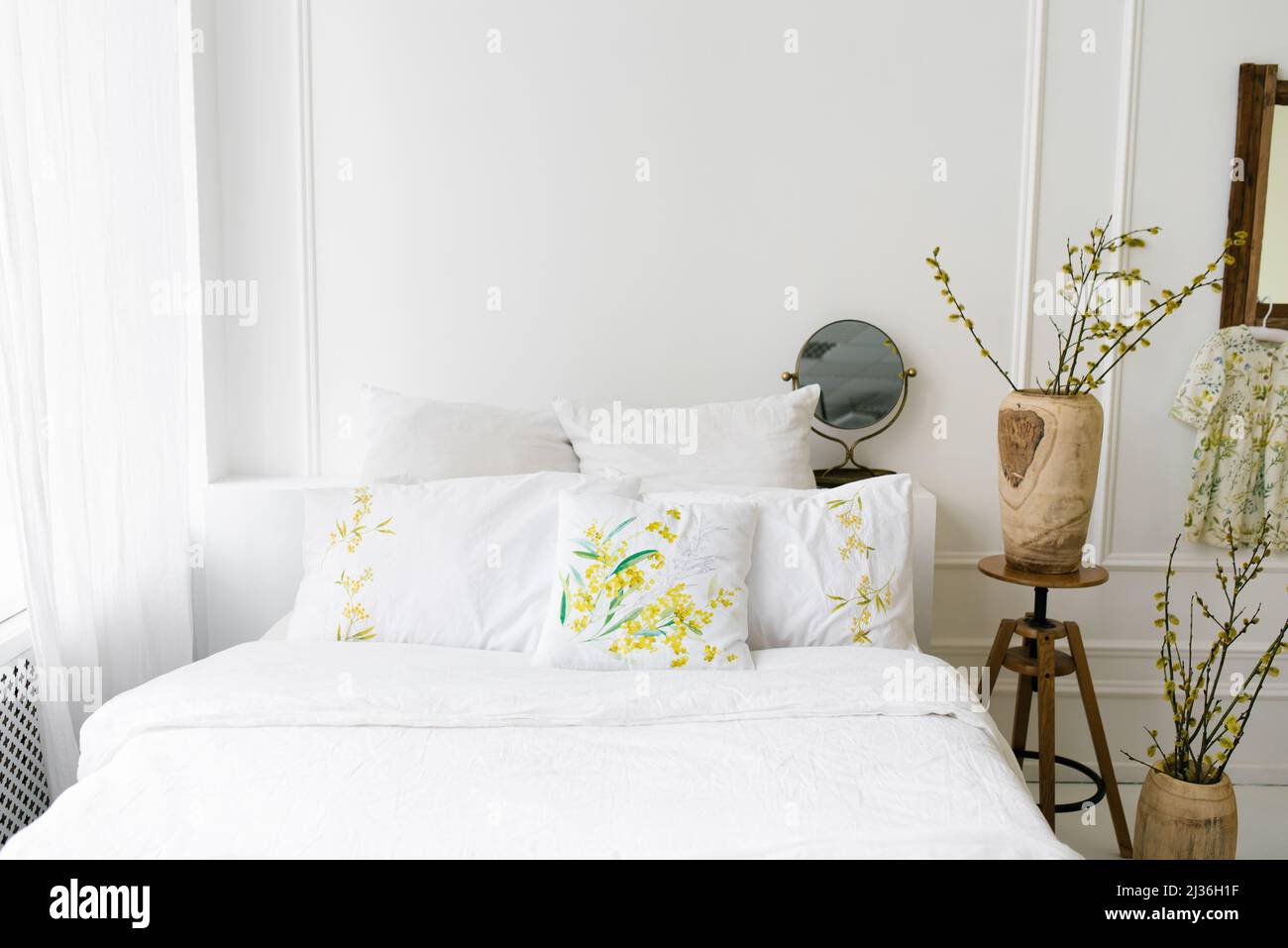 Light airy white with yellow shades bedroom in the house. Cozy bed and vases with spring branches Stock Photo