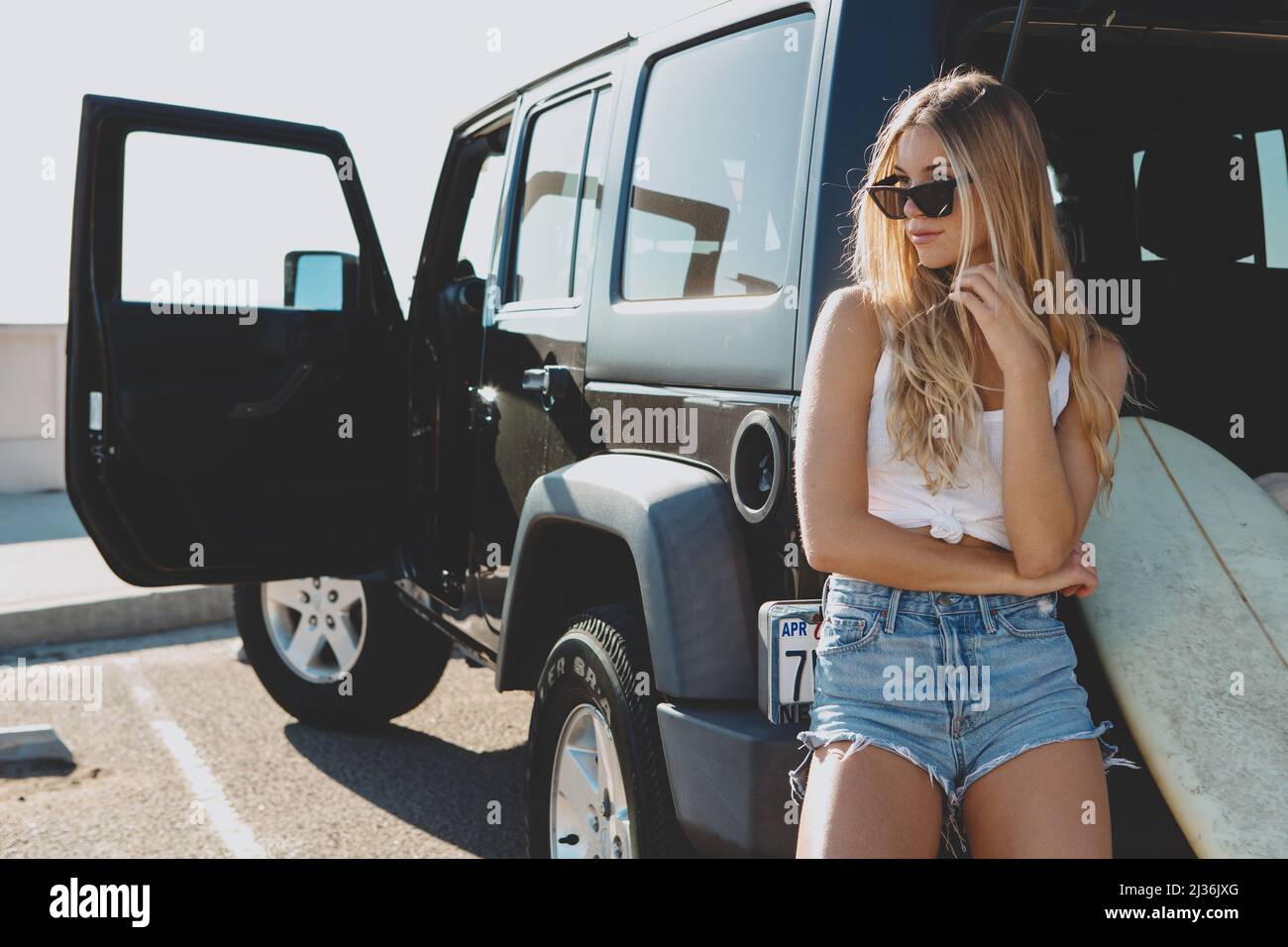 surfer girl sitting at a car with surfboard. On film California Stock Photo