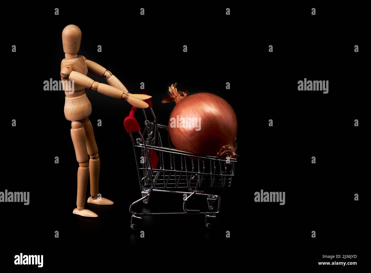 Dummy pushing a shopping cart with an onion on black background. Trade symbol. Healthy shopping Stock Photo